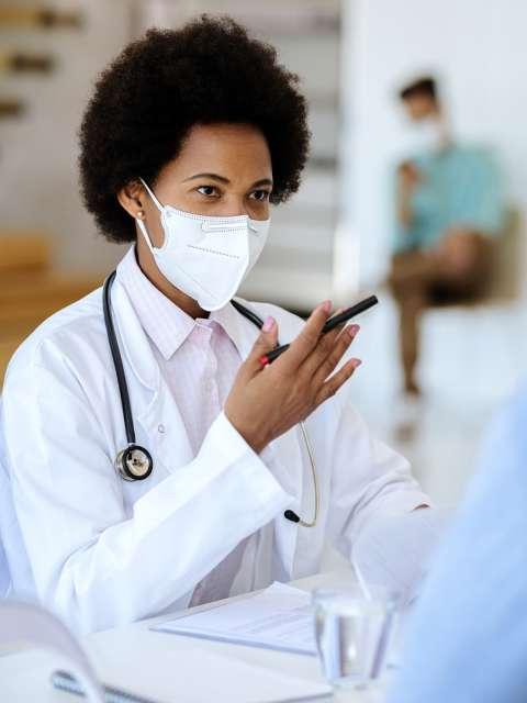 Masked Black female doctor talking to patients.